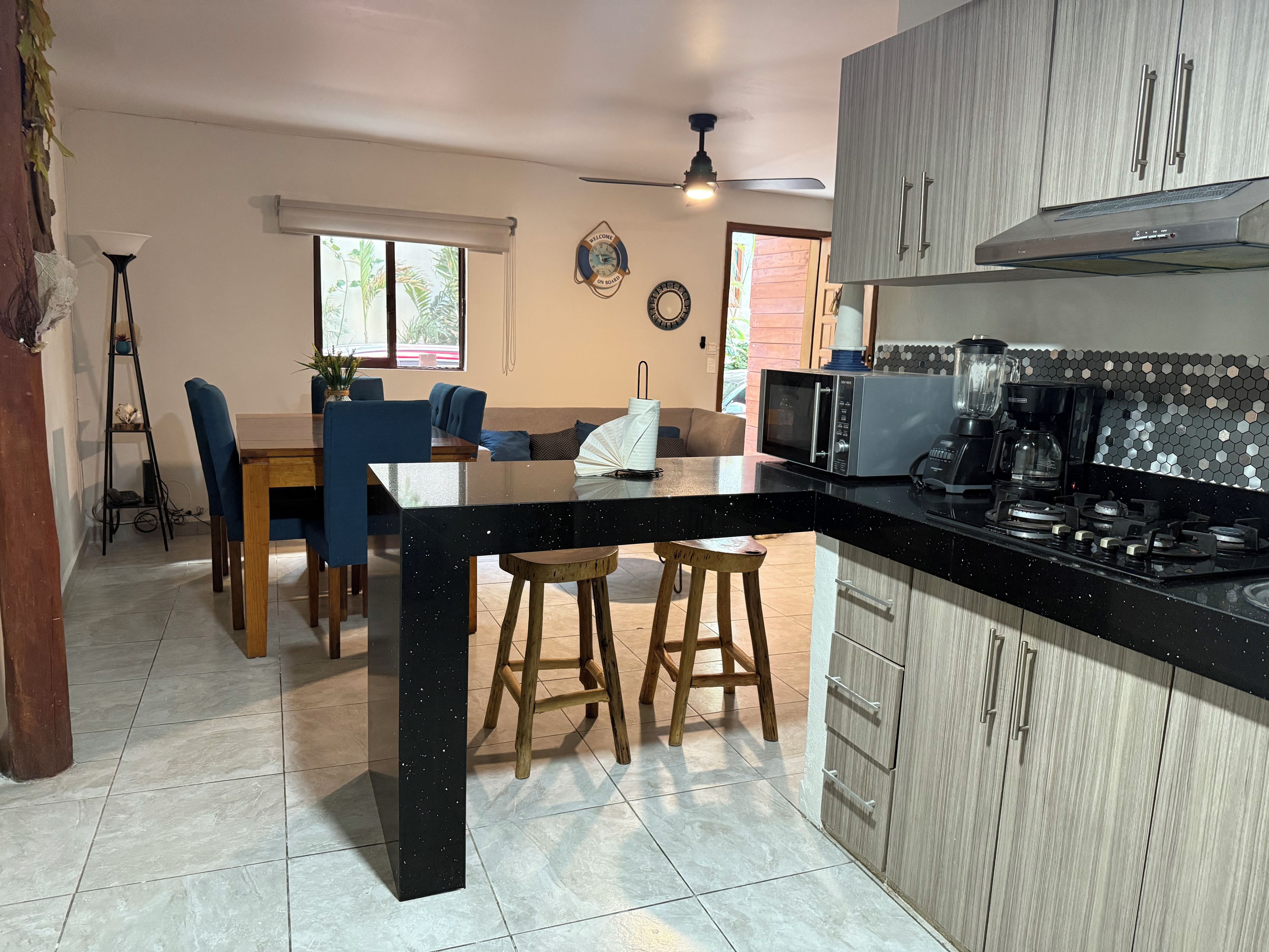 A modern kitchen with a black countertop, wooden chairs, a dining table, and a ceiling fan.