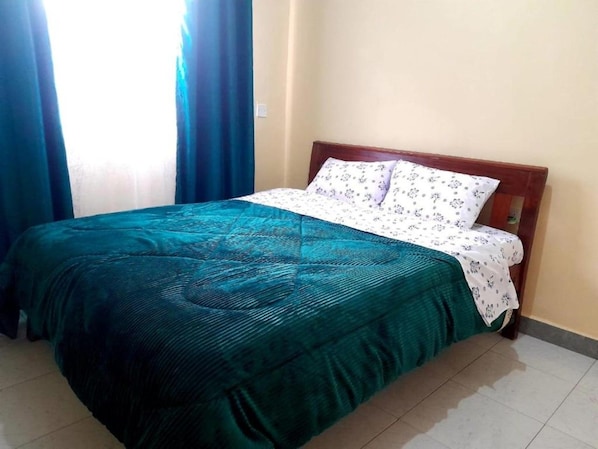 Una cama individual con cabecera de madera en una habitación con suelo de baldosas.