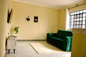 Une pièce avec un canapé vert, un bureau blanc orné d’une plante et deux tableaux accrochés au mur.