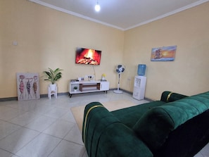 A living room with a sofa, TV, fan, and artwork on the wall.