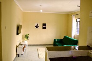 Una sala de estar con un sofá verde, un televisor de pantalla plana montado en la pared y un ventanal con cortinas.