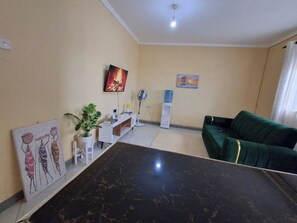 A living room with a black marble coffee table, a green sofa, a white cabinet, a painting, and a fan.