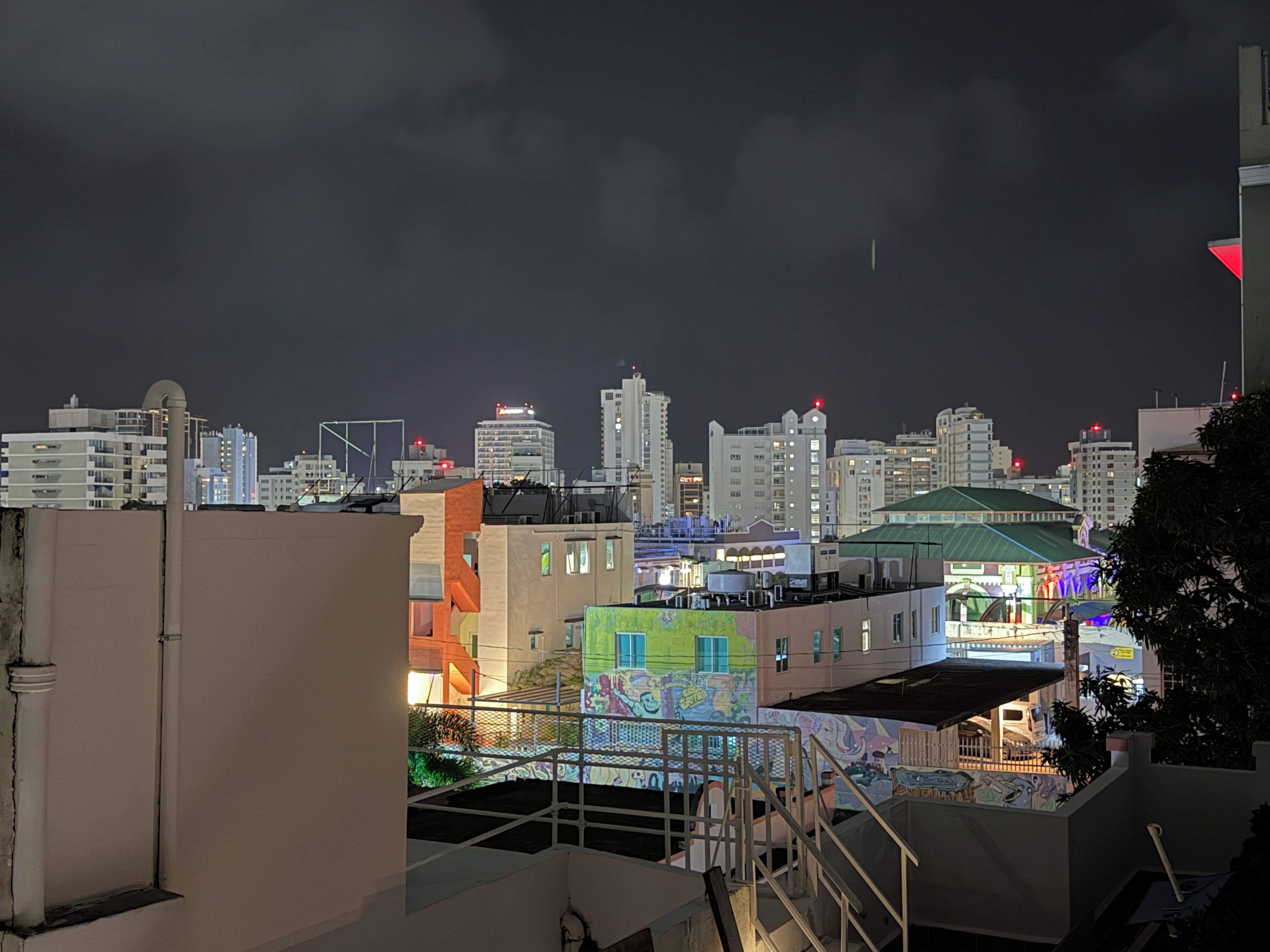Une vue nocturne d’une ville, avec des bâtiments et une terrasse sur le toit.