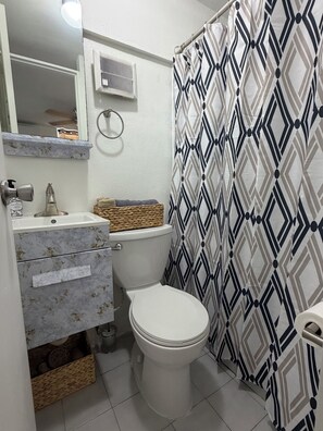 Een badkamer met toilet, wastafel, spiegel en een douchegordijn met een geometrisch patroon.