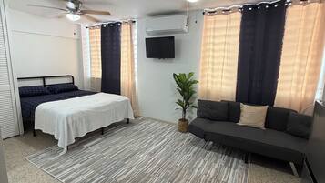 Une chambre à coucher moderne avec un lit, un canapé, un téléviseur et un ventilateur de plafond.