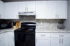 A kitchen with white cabinets, a black stove, a microwave, and a granite countertop.