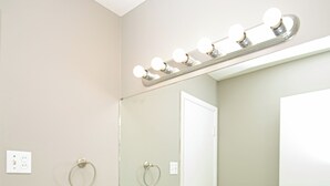 Une salle de bain avec un lavabo blanc, un meuble-lavabo et un miroir surmonté de luminaires.