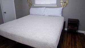 Une chambre à coucher avec un lit, une fenêtre avec des stores, une porte et une petite table de chevet.