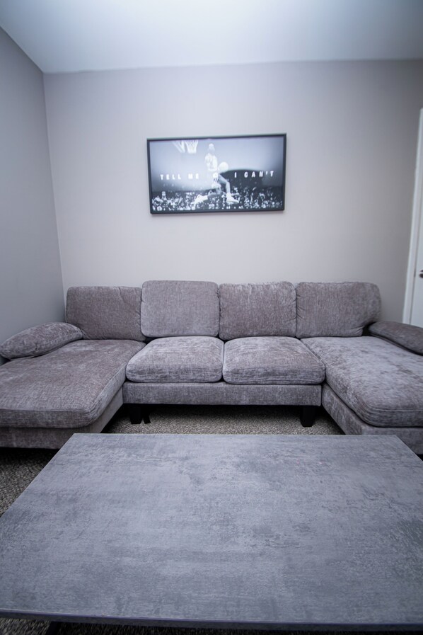 A living room with a grey sectional sofa, a grey coffee table, and a framed picture on the wall.
