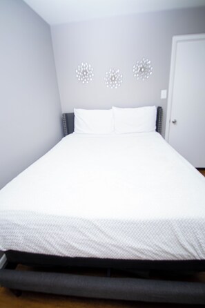 Une chambre avec un lit simple, un mur gris, une porte blanche et un lit doté d’un matelas blanc et d’une tête de lit grise.