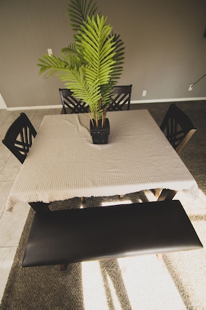 Une table à manger recouverte d’une nappe tissée, agrémentée d’une plante en pot et entourée de quatre chaises.