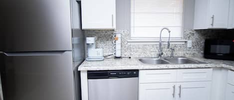 Una cocina con refrigerador de acero inoxidable, cafetera, lavavajillas, pileta y microondas.