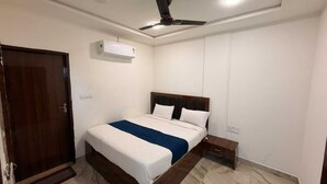 A bedroom with a bed, a ceiling fan, an air conditioning unit, a wooden door, and a bedside table. - Om Home Stay (Mayapura)