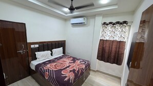 A bedroom with a bed, a ceiling fan, an air conditioning unit, and a window with curtains. - Om Home Stay (Mayapura)