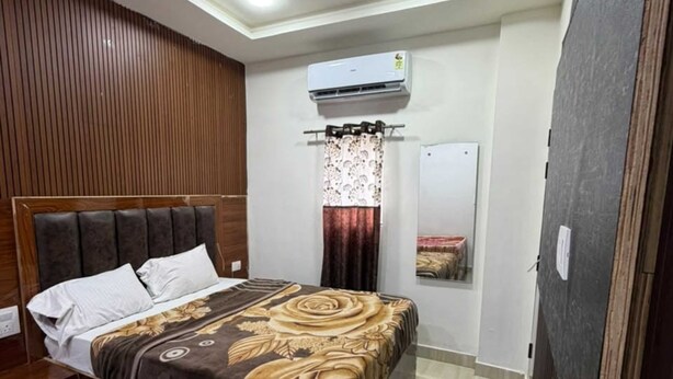 A bedroom with a bed, a ceiling fan, an air conditioning unit, a window with curtains, and a mirror. - Om Home Stay (Mayapura)