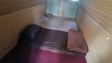 A narrow room with wooden paneling on the walls, a bed with a brown blanket and pillows, and a red carpet on the floor.