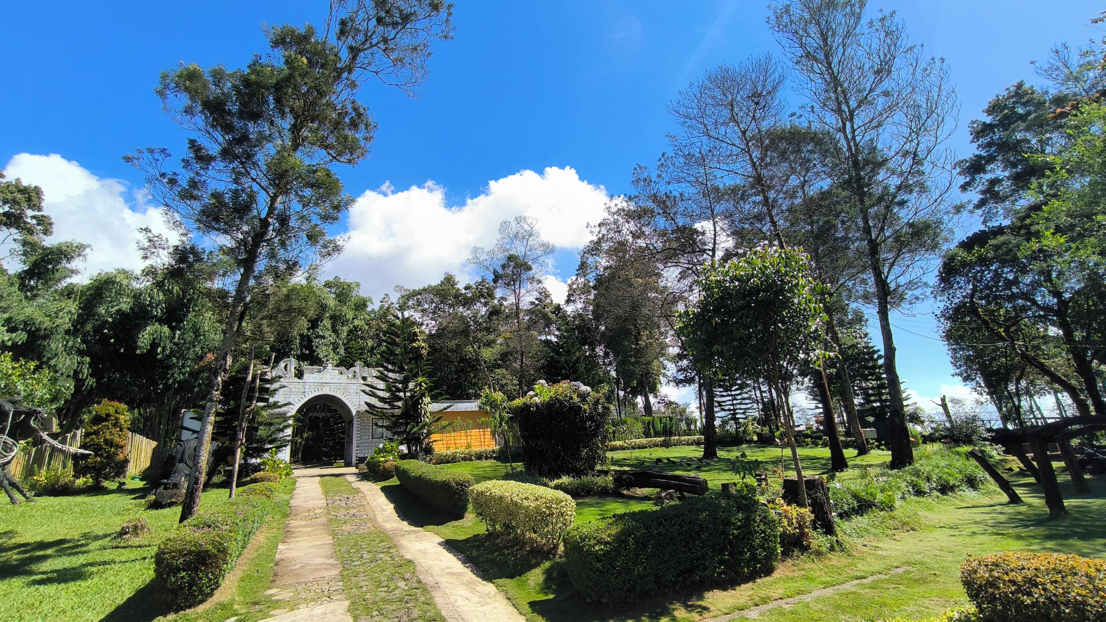A pathway leading to a stone archway surrounded by lush greenery and trees.