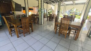A covered outdoor dining area with wooden tables and chairs, a tiled floor, and a view of greenery in the background. - Merbabu Park (Kabupaten Semarang)