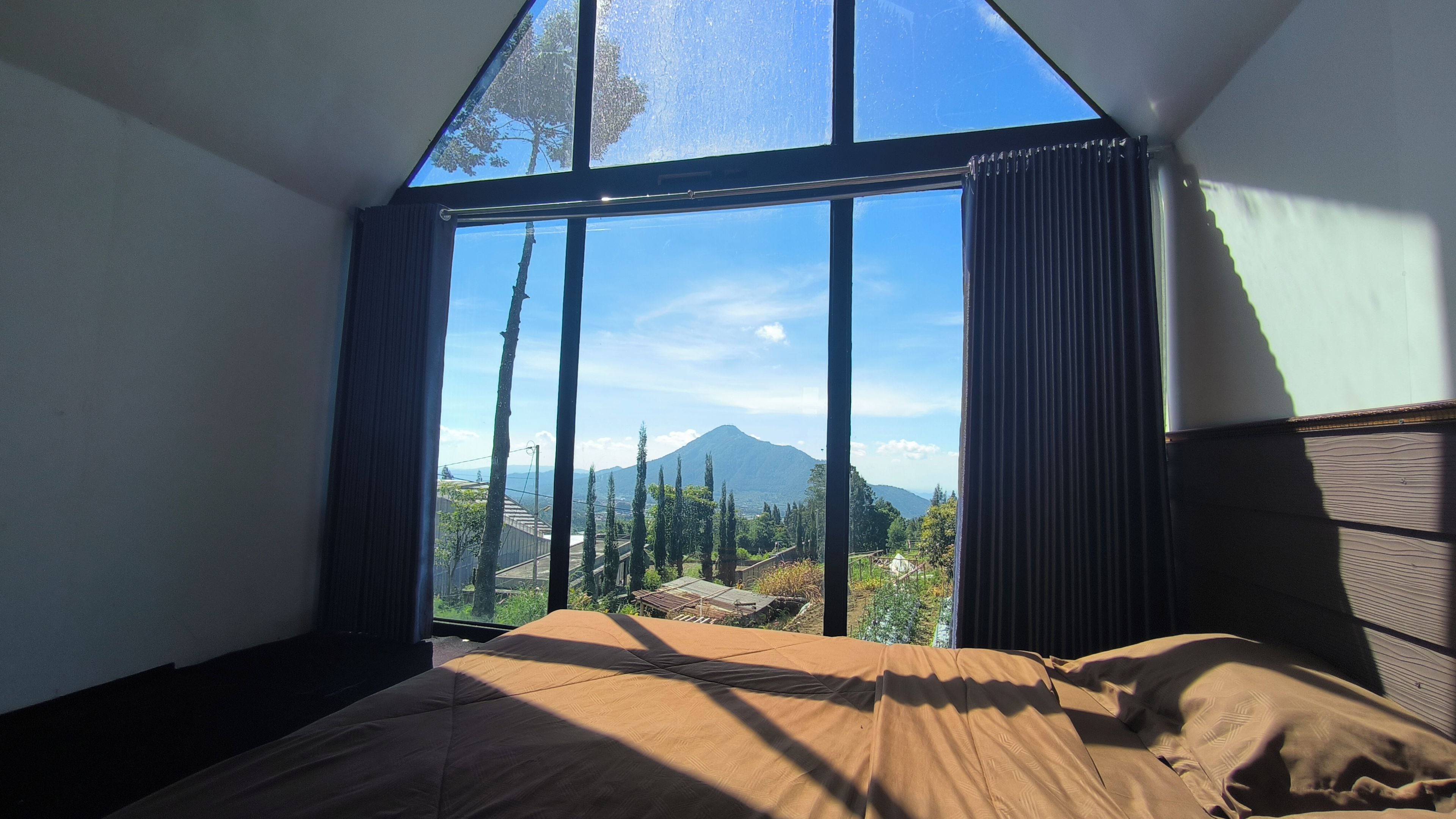 A bedroom with a large window, a bed, and a view of a mountain.