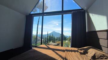 A bedroom with a large window, a bed, and a view of a mountain.
