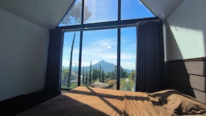 A bedroom with a large window, a bed, and a view of a mountain.