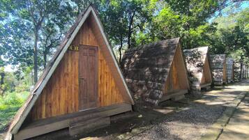 A row of wooden A-frame cabins with a door and a sign, surrounded by trees.