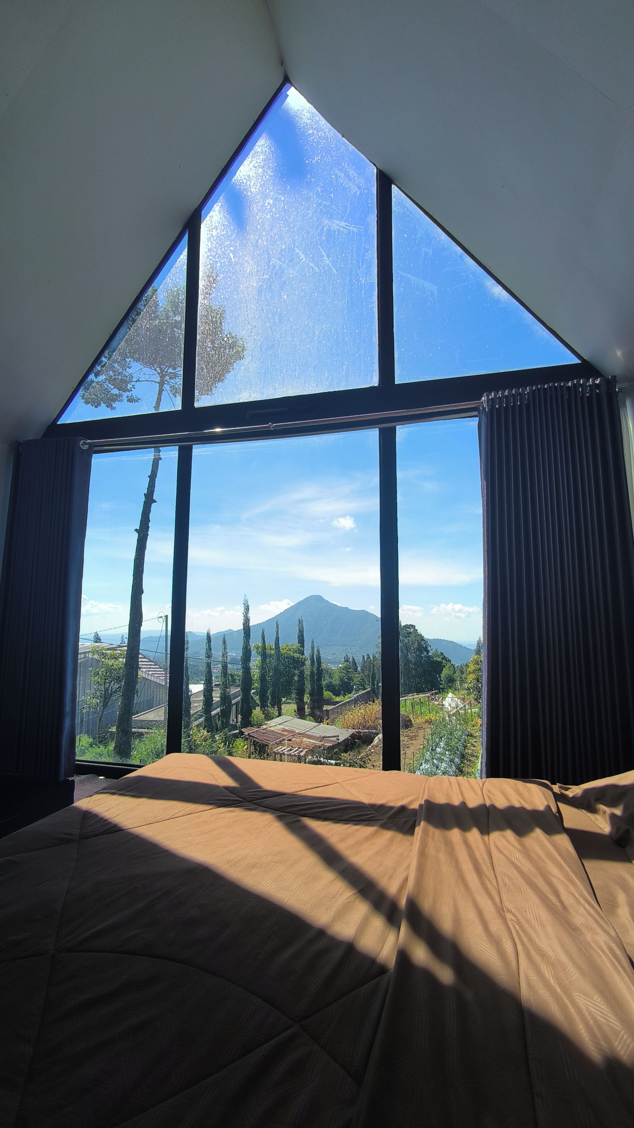 A room with a large window, a bed, and a view of a mountain.