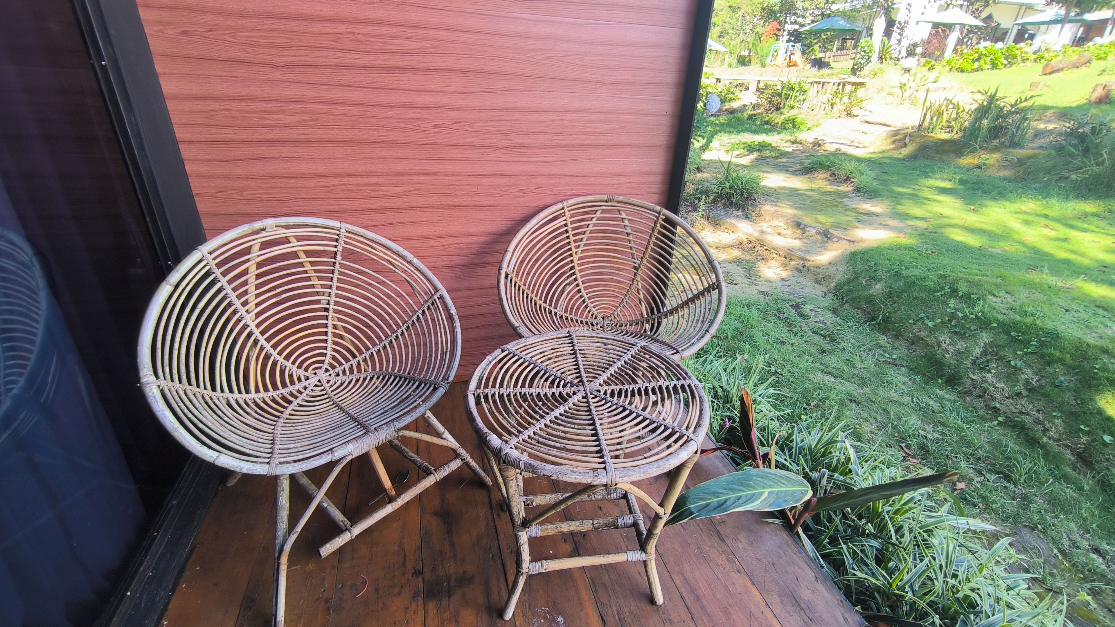 Una terraza de madera con tres sillas de mimbre y una planta en maceta.