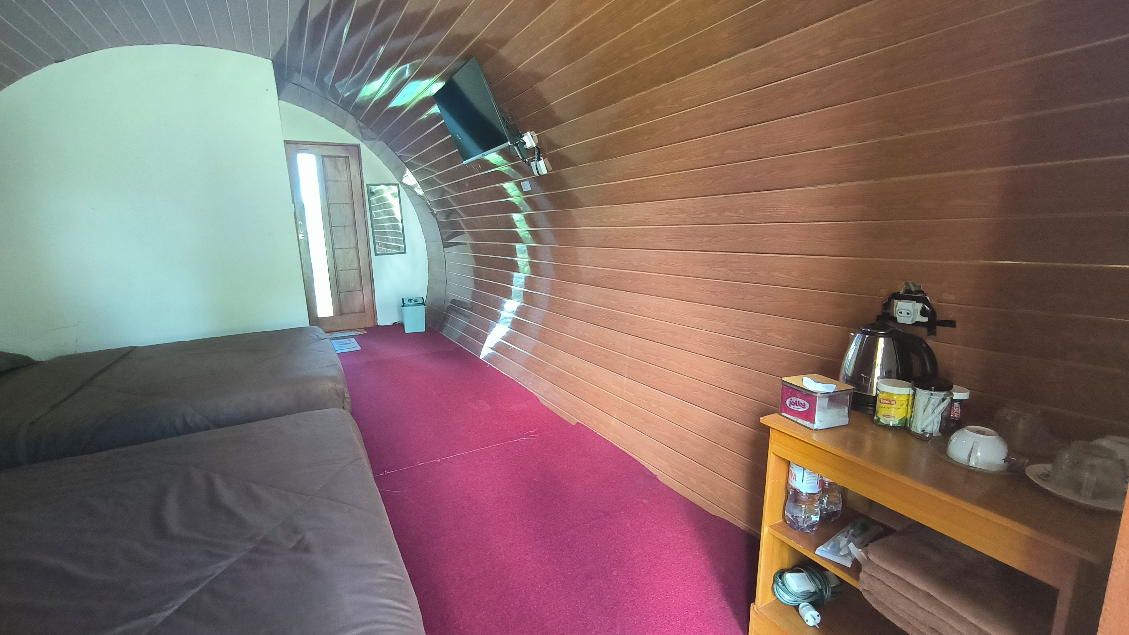 A room with a bed, a wooden shelf with items, and a red carpet.