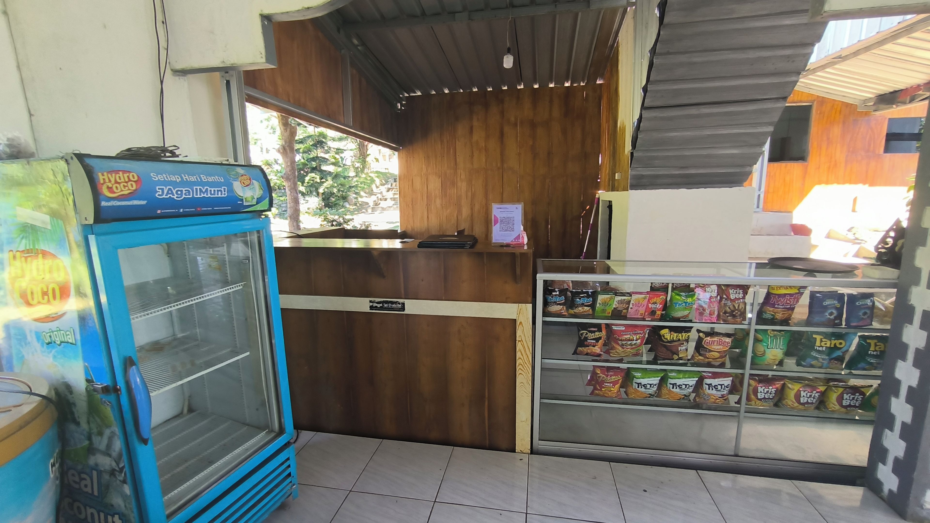 A small shop with a blue refrigerator, a wooden counter, and a snack display.