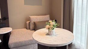 A modern hotel room with a sofa, a round table with a vase of flowers, a painting on the wall, and a window with curtains. - WUHAN BOLEST HOTEL (Wuhan)