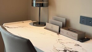 A modern desk with a marble top, a black chair, a desk lamp, a charging station, and a remote control. - WUHAN BOLEST HOTEL (Wuhan)