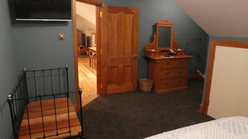 A bedroom with a bed, a wooden dresser, a mirror, a television on the wall, and a door leading to another room.