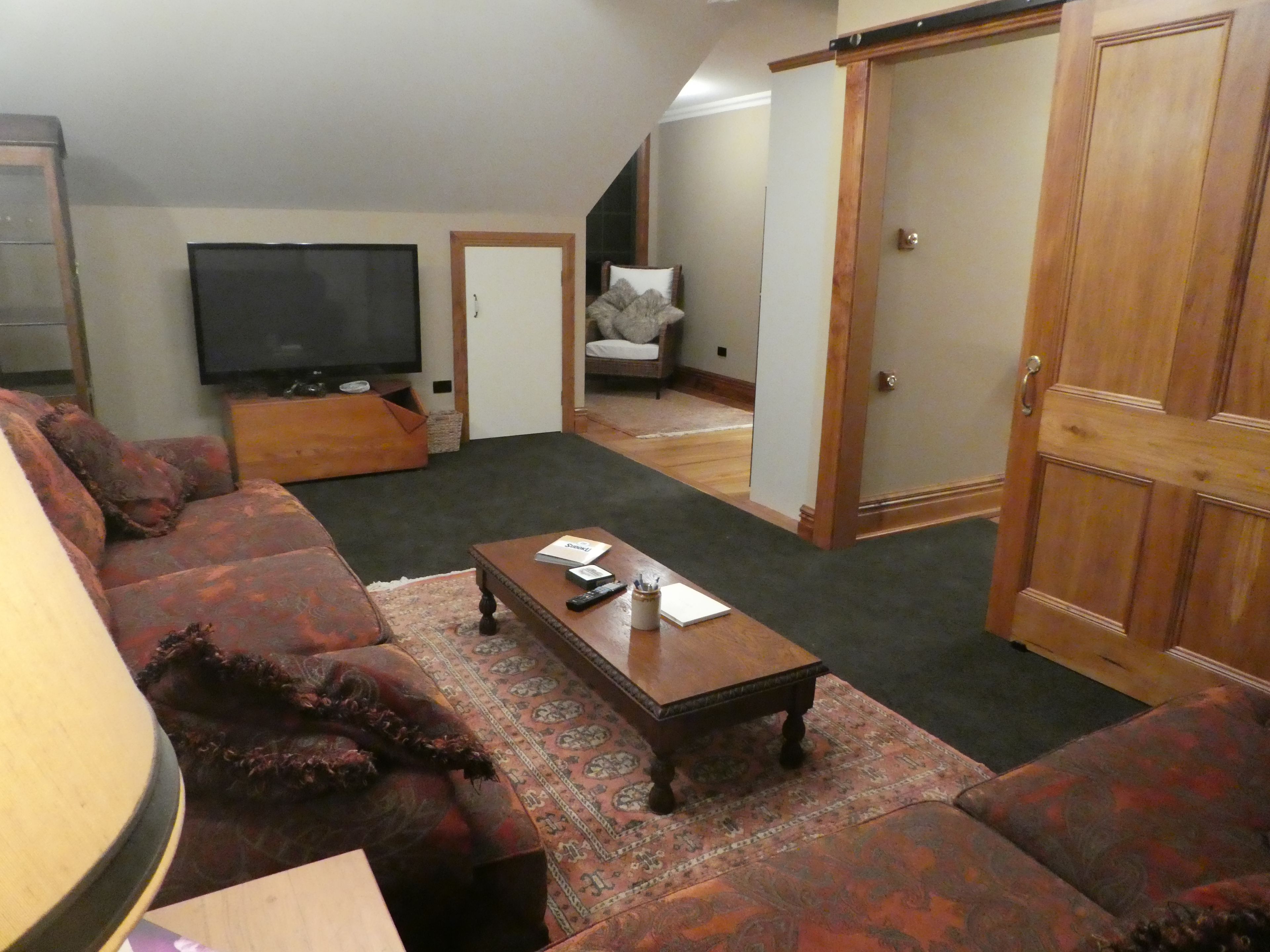 Una sala de estar con un sofá, una mesa de centro, un televisor y una puerta que da a otra habitación.