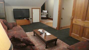 Una sala de estar con un sofá, una mesa de centro, un televisor y una puerta que da a otra habitación.