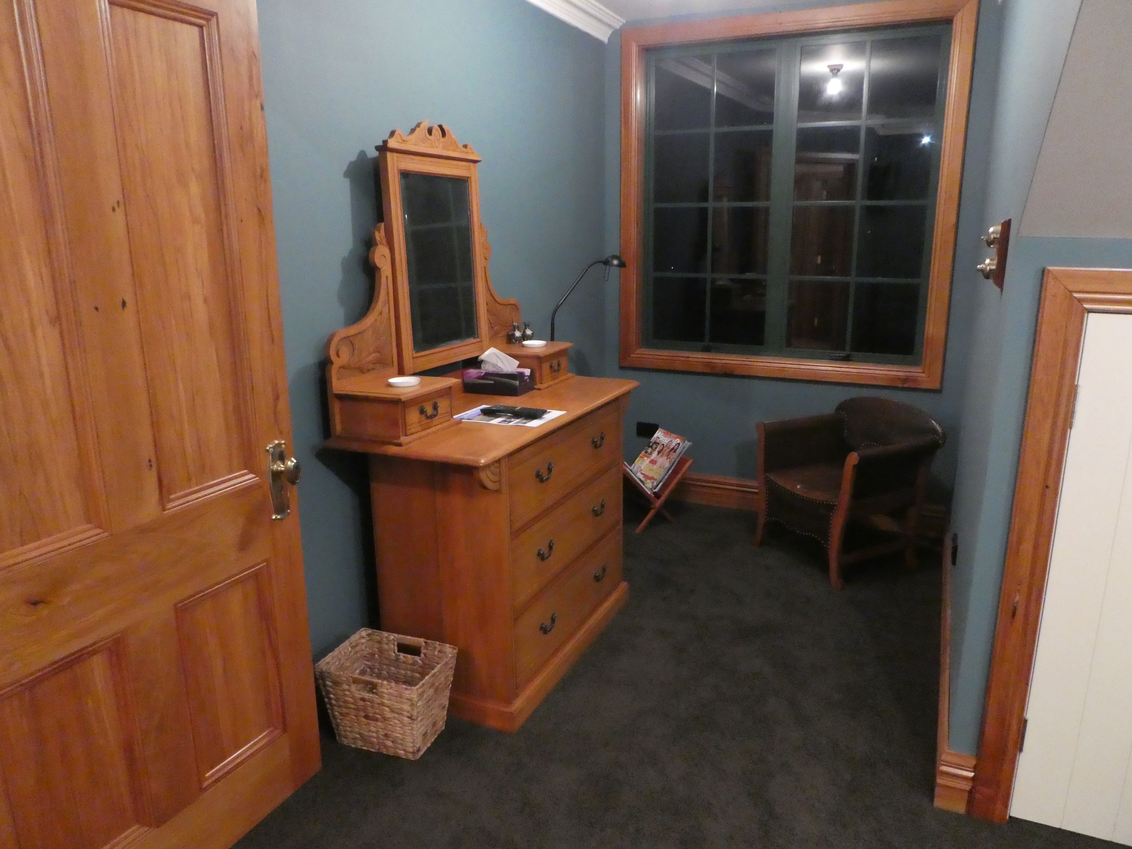 A room with a wooden dresser, a mirror, a chair, and a window.