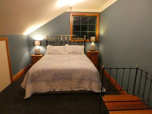 A bedroom with a bed, two bedside tables, a nightstand, a window, and a staircase. - KAWAU VILLA - 5 star upstairs private apartment (Palmerston North)