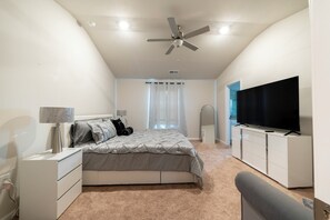 A bedroom with a bed, a TV, a ceiling fan, and a window with curtains. - Modern Oasis (Charlotte)