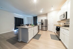 A modern kitchen with a central island, stainless steel appliances, and light wood flooring. - Modern Oasis (Charlotte)