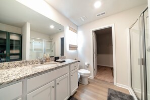 A modern bathroom with a granite countertop, a glass shower enclosure, and a walk-in closet. - Modern Oasis (Charlotte)