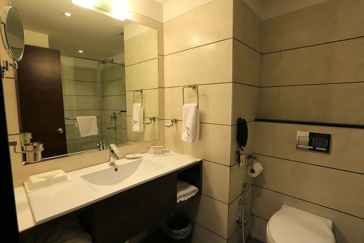 A modern bathroom with a large mirror, two sinks, a toilet, and a shower.