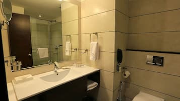 A modern bathroom with a large mirror, two sinks, a toilet, and a shower.