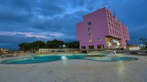 A modern building with a pool area, featuring a large rectangular pool and a smaller circular pool, surrounded by a tiled deck. - Nandankanan Hotel & Resorts  (Lohar Pipalya)
