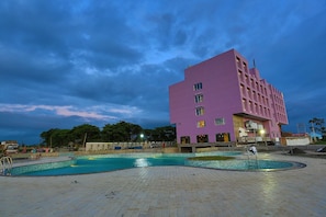 Ein modernes Gebäude mit Poolanlage, inklusive eines großen rechteckigen Pools und einem kleineren runden Pool, umgeben von einer gefliesten Terrasse.