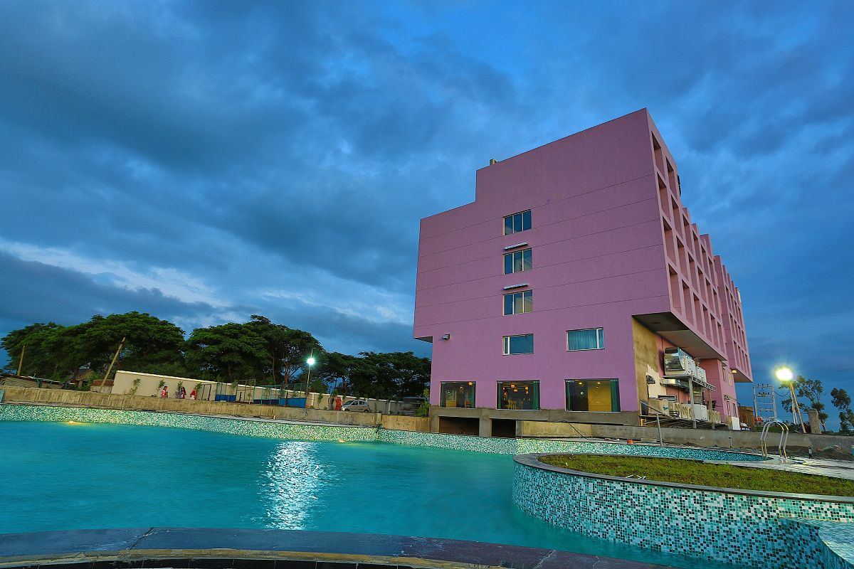 Un bâtiment moderne avec une piscine à l’avant, entouré d’arbres et sous un ciel dégagé.