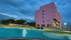 A modern building with a pool in front, surrounded by trees and a clear sky. - Nandankanan Hotel & Resorts  (Lohar Pipalya)