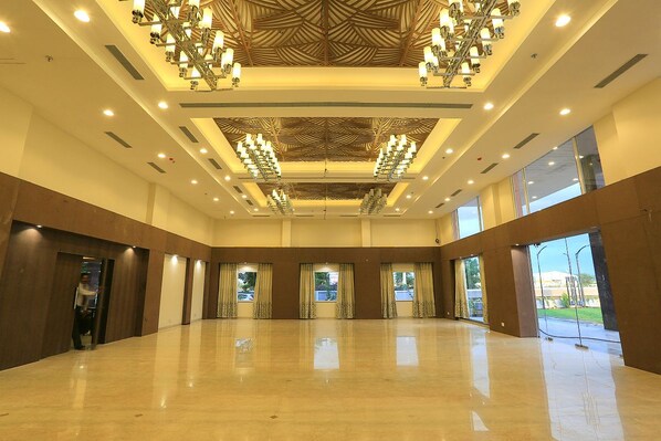 A spacious hotel lobby with a high ceiling, large windows, and a central chandelier.