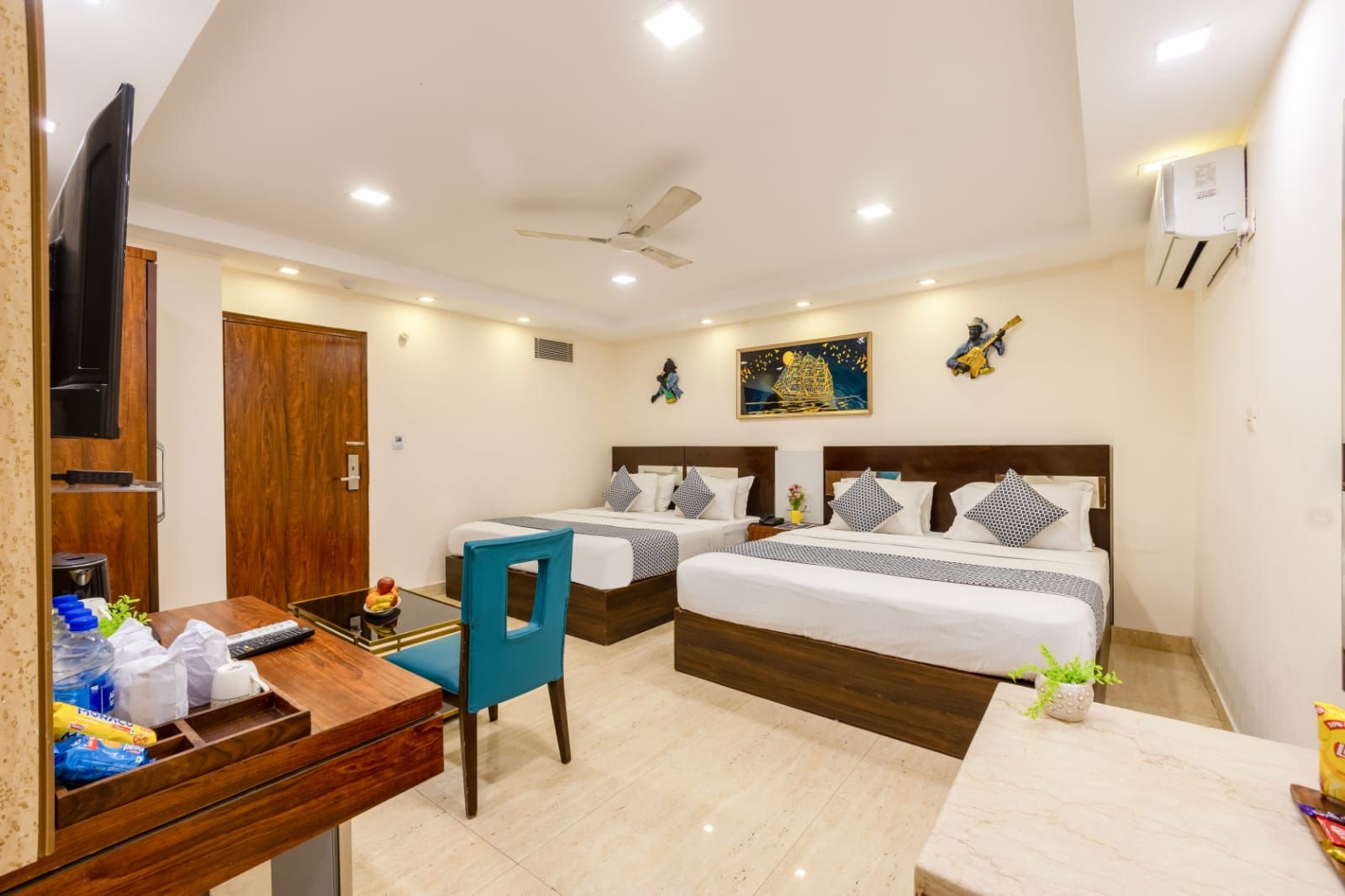 A hotel room with two beds, a desk with a chair, a TV, and a ceiling fan.