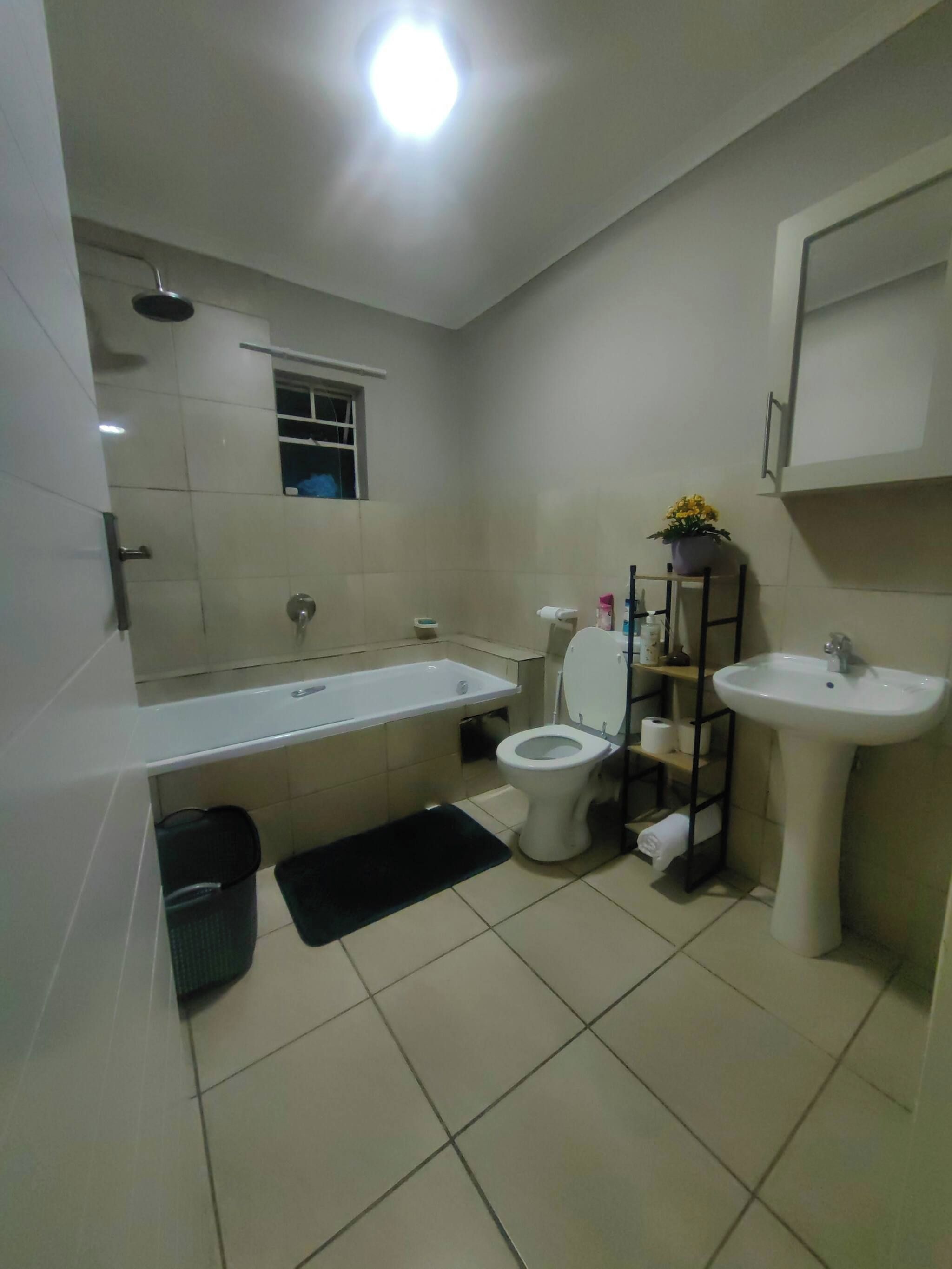 A modern bathroom with a bathtub, toilet, sink, and a small window.