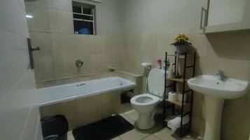 A modern bathroom with a bathtub, toilet, sink, and a small window.